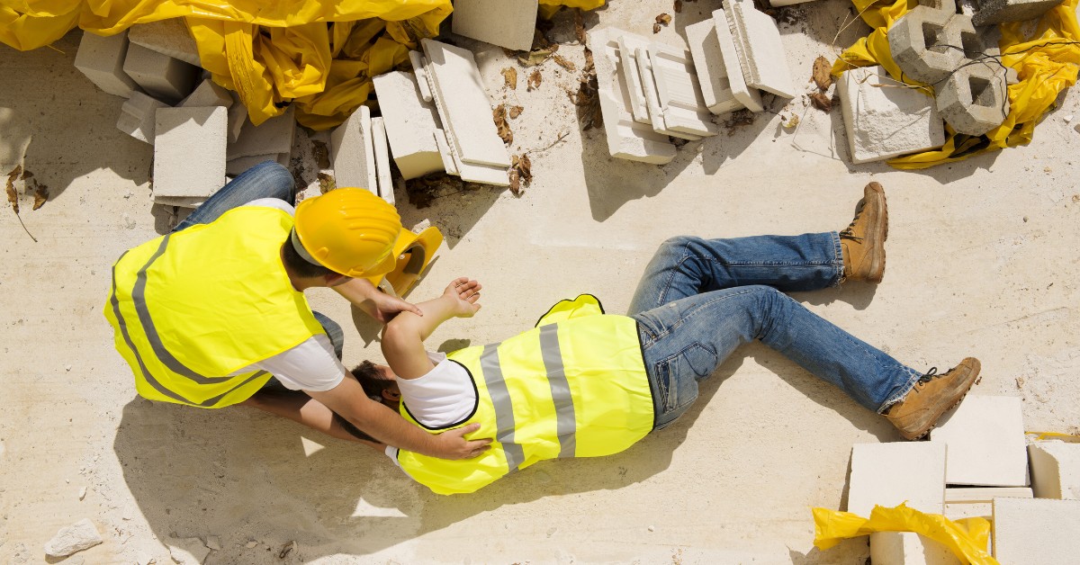 A construction worker assists an injured coworker lying among debris at a construction site.