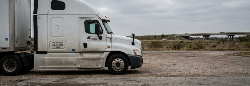 DOT-labeled semi-truck with trailer parked near highway overpass