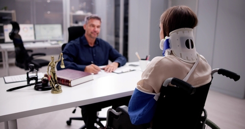 injured worker in wheelchair with neck brace meeting attorney at desk
