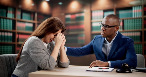 Woman covering face while speaking with lawyer at desk, law books behind