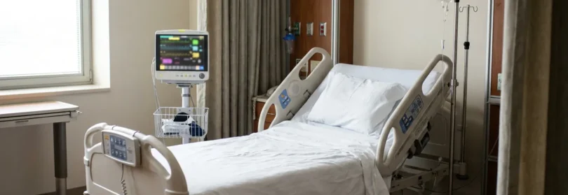empty hospital bed with patient monitor and IV stand in private room