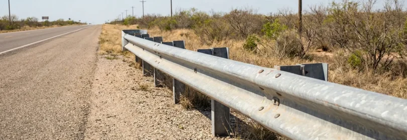 metal guardrail along rural highway shoulder with sparse desert vegetation